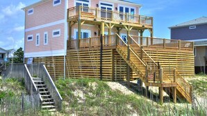Een meerlaags huis aan het strand met een houten terras en een trap.