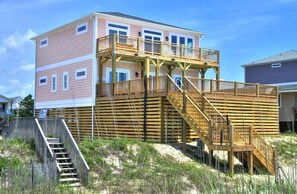 Una casa frente a la playa de varios pisos con una terraza de madera y escaleras.