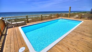 Een houten terras met een zwembad en uitzicht op de oceaan.