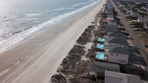 Luchtbeeld van een kustgebied met een strand, huizen en een zwembadcomplex.