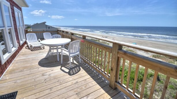 A wooden deck with a table and chairs overlooking a beach. - Experience oceanfront luxury at 'No Worries,' an ideal 5-bedroom retreat in Oak Island. (Oak Island)