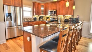 A modern kitchen with wooden cabinets, stainless steel appliances, a granite countertop, and pendant lighting. - Experience oceanfront luxury at 'No Worries,' an ideal 5-bedroom retreat in Oak Island. (Oak Island)