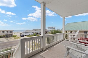 A beachfront property with a covered porch, a view of the beach, and a row of beach houses.