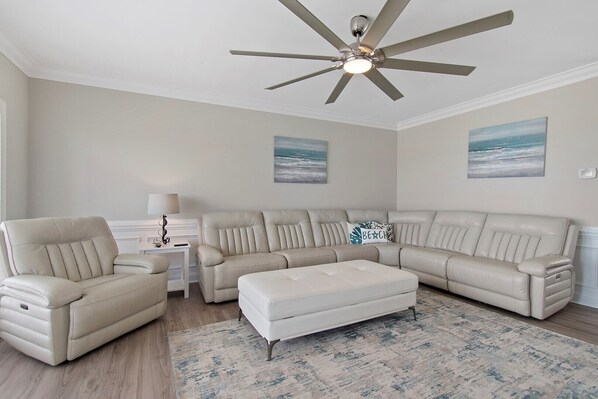 A living room with a sectional sofa, a chaise lounge, a ceiling fan, and a rug.