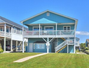 A two-story house with a balcony, a covered porch, and a staircase leading to the upper level. - Experience coastal living at Ocean Breeze Retreat in Oak Island with ocean views. (Oak Island)