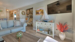 A living room with a light blue sofa, a wooden coffee table, a white console table with a sailboat model, and a vase with red coral.