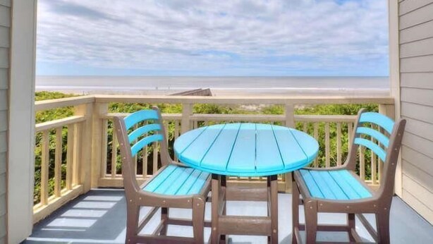 A covered outdoor area with a round table and four chairs, overlooking a beach.