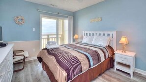 A bedroom with a bed, a desk, a chair, a nightstand, and a ceiling fan.