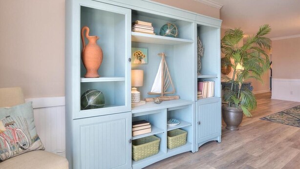 Un mueble de madera azul claro con estantes y cajones, que contiene libros, objetos decorativos y cestas de mimbre.