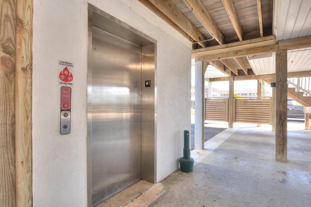 Un ascenseur avec un panneau indiquant les escaliers de secours, un plancher en béton et des poutres en bois.