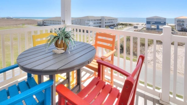 Varanda com mesa e cadeiras, vista para a praia e edifícios.