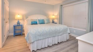 Quarto com cama, duas mesas de cabeceira com luminárias, ventilador de teto e janela com persianas.