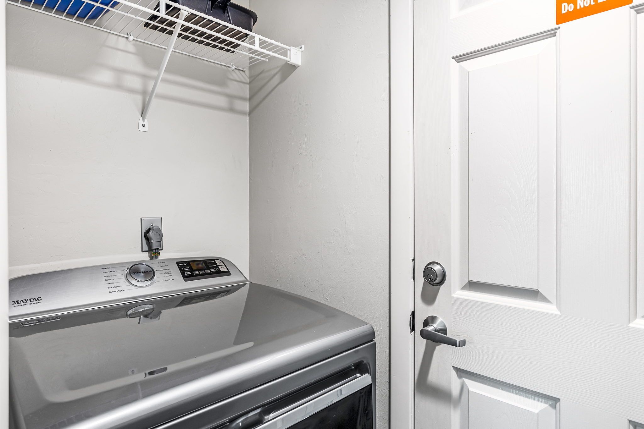 A laundry room with a Maytag dryer, a white door with a do not enter sign, and a wall-mounted drying rack.