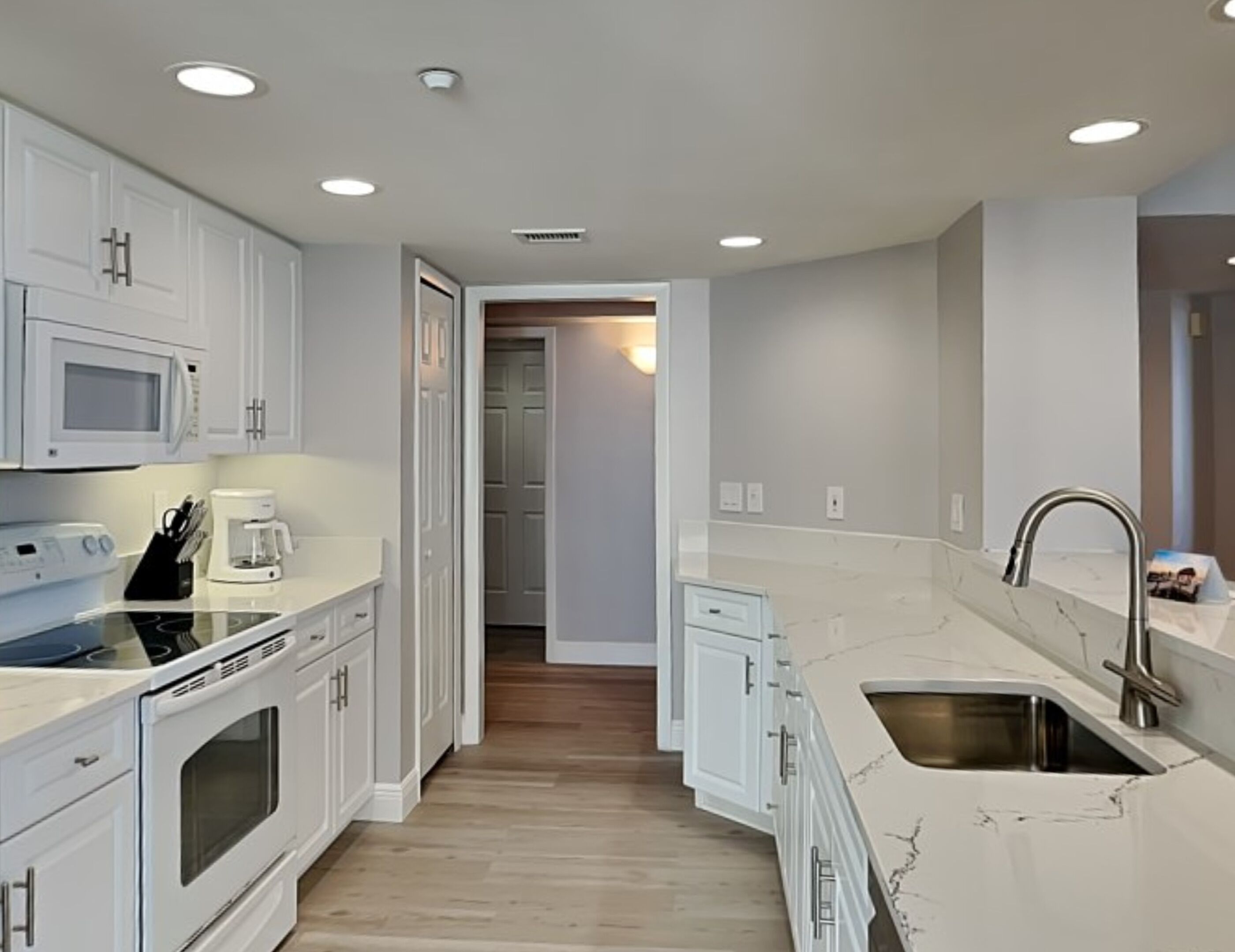 A modern kitchen with white cabinetry, a built-in oven, a microwave, and a coffee maker.