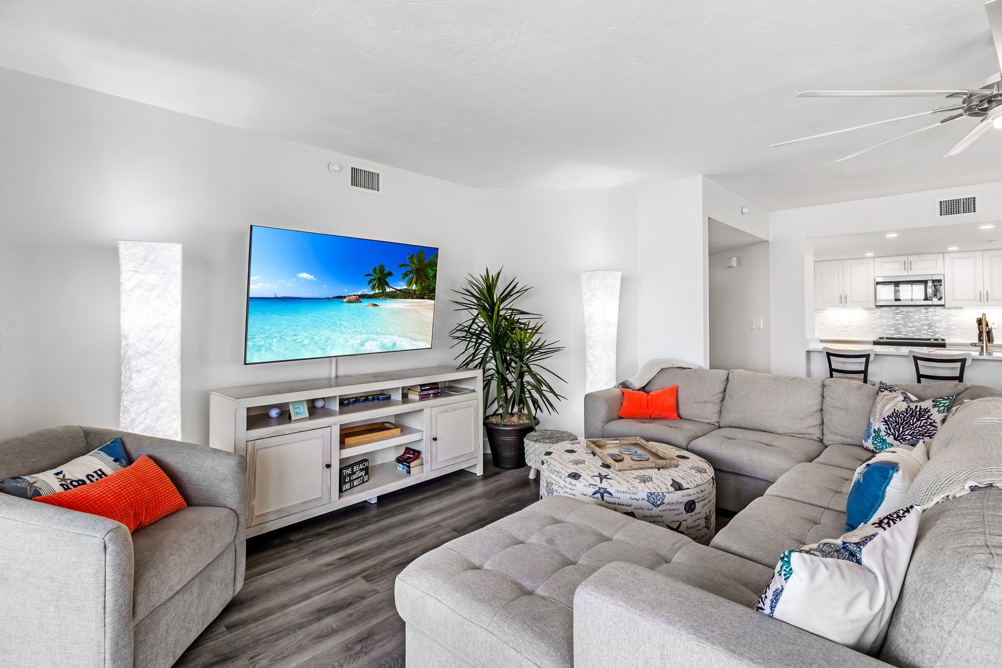 Una sala de estar moderna con un televisor de pantalla plana, sofás grises, un mueble de entretenimiento blanco y una planta en maceta.