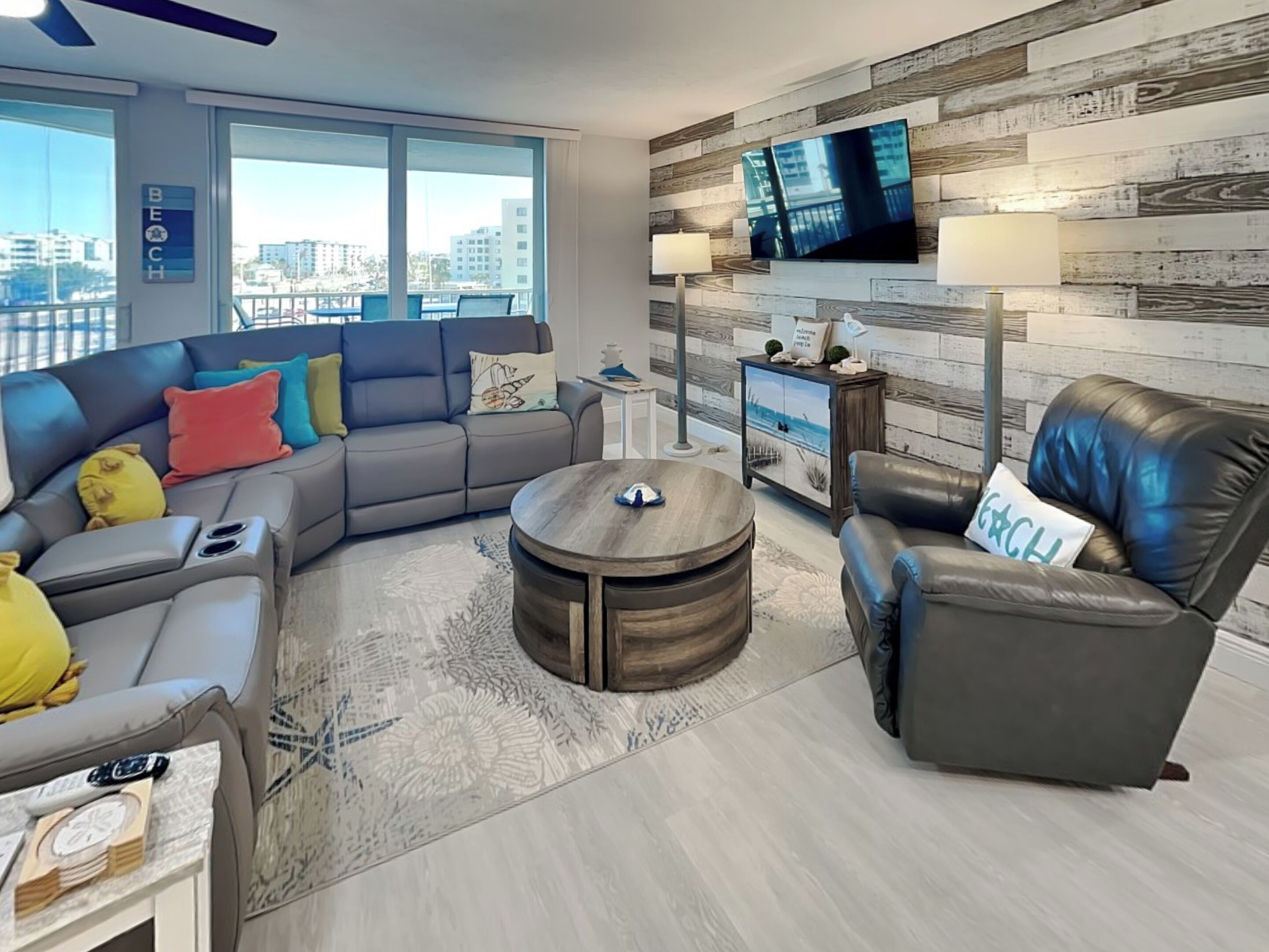 A modern living room with a sectional sofa, a round coffee table, a leather armchair, and a TV mounted on a wooden wall.