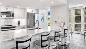 Uma cozinha moderna com armários brancos, eletrodomésticos de aço inoxidável e uma ilha central com banquetas.
