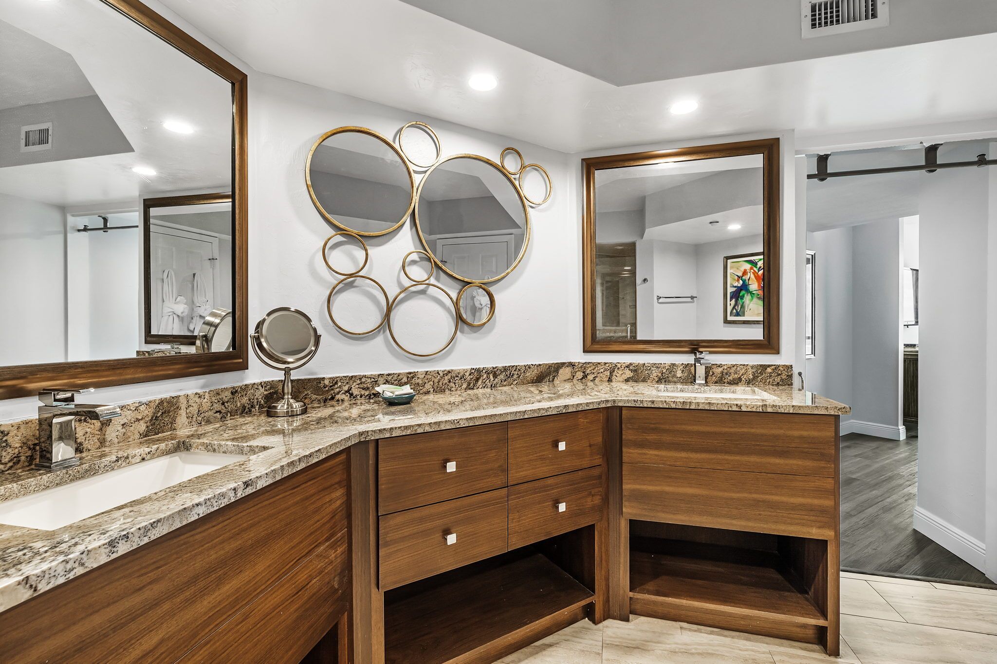 A modern bathroom with a granite countertop, wooden vanity, and multiple mirrors.
