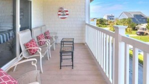 A covered porch with white railings, a row of white chairs with red cushions, and a small table.