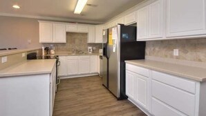 A modern kitchen with white cabinetry, a stainless steel refrigerator, and a light wood floor.