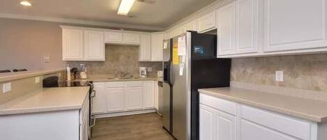 A modern kitchen with white cabinetry, a stainless steel refrigerator, and a light wood floor.