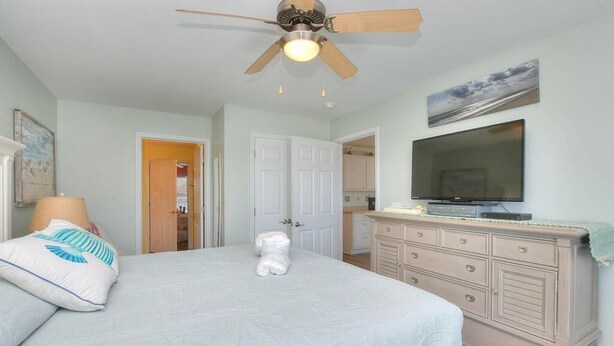 Une chambre à coucher comprenant un lit, un ventilateur de plafond, une commode et un téléviseur.