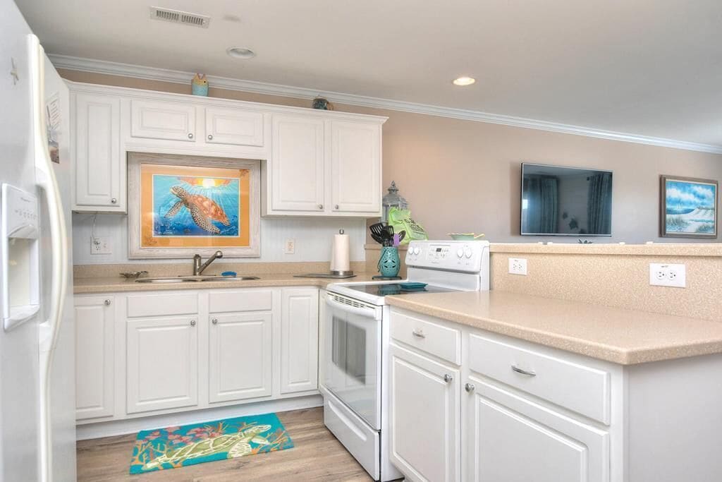 A kitchen with white cabinets, a stove, a sink, and a microwave.