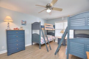 A room with bunk beds, a dresser, a ceiling fan, and a window with blinds.