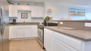 A kitchen with white cabinets, a stainless steel refrigerator, a double oven, granite countertops, and a small island with a sink. - Stay at Beach Pals in Oak Island—spacious condo with ocean views, sleeps 10! (Oak Island)