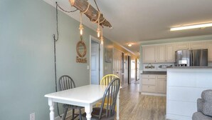 A dining area with a white table and chairs, a kitchen with white cabinets and stainless steel appliances, and a hallway leading to another room. - Experience ocean views at Oak Island OW 3204, a spacious 3-bedroom condo ideal for 10 guests. (Oak Island)