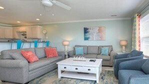 A living room with a grey sofa, a white coffee table, and a blue armchair. There is a painting on the wall and a window with blinds. - Experience ocean views at Oak Island OW 3204, a spacious 3-bedroom condo ideal for 10 guests. (Oak Island)