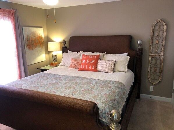 Une chambre à coucher avec un grand lit, une table de chevet, une lampe, un élément décoratif mural et une fenêtre avec des rideaux.