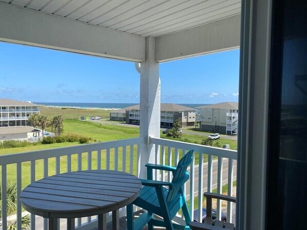 A balcony with a table and chairs, overlooking a residential area and the ocean.