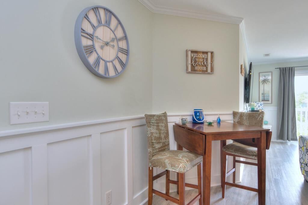A dining area with a wooden table and two chairs, a wall clock, and a welcome sign.