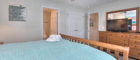 Een slaapkamer met een bed, een plafondventilator, een dressoir, een televisie en een deur naar een andere kamer.