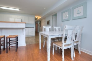 A kitchen with white cabinets, a wooden countertop, a white table with chairs, and a hallway with framed pictures on the wall. - Oceanview condo in Oak Island, featuring 3 bedrooms and 2 bathrooms. (Oak Island)