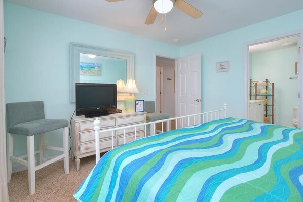 A bedroom with a bed, a television, a dresser, a chair, and a ceiling fan.