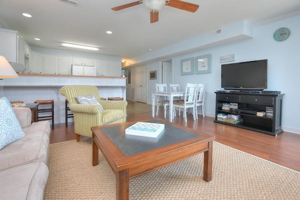 A living room with a sofa, armchair, coffee table, TV, and a dining area with chairs and a table. - Oceanview condo in Oak Island, featuring 3 bedrooms and 2 bathrooms. (Oak Island)