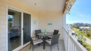 Een overdekt terras met een glazen deur naar een zwembad, een ronde tafel met stoelen en uitzicht op de wijk.
