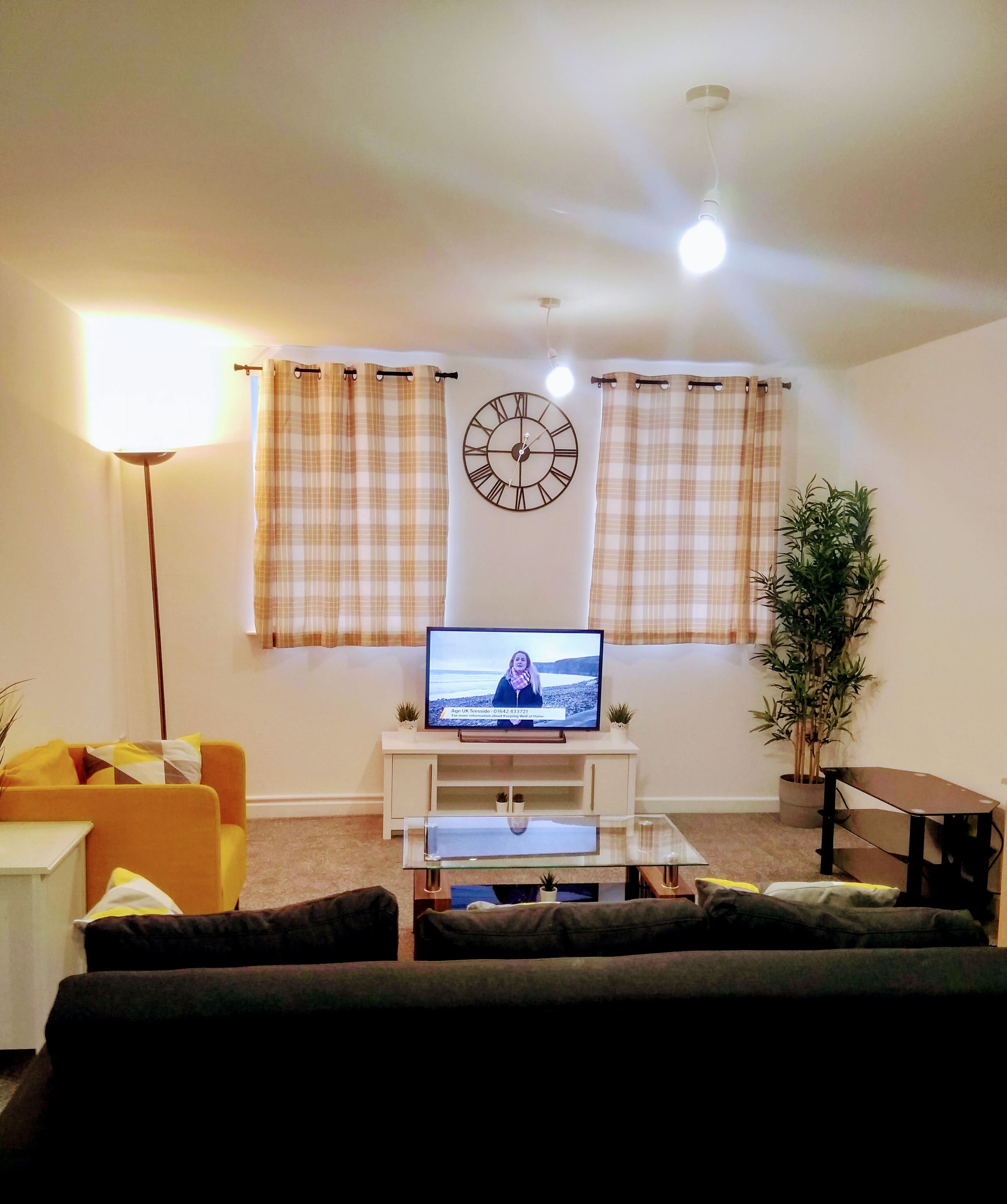A living room with a television, a clock, a sofa, a lamp, and a plant.