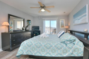 A bedroom with a bed, a ceiling fan, a dresser, a TV, and a large window.