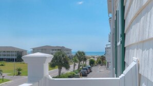 A balcony with a view of a beach, parked cars, and buildings in the background. - Relax in this oceanview condo in Oak Island, featuring 2 bedrooms for 6 guests. (Oak Island)