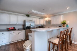 A kitchen with white cabinets, a stainless steel refrigerator, a microwave, and a small island with bar stools.