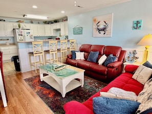 A living room with a red sofa, a coffee table, and a dining area with wooden chairs and a white cabinet.
