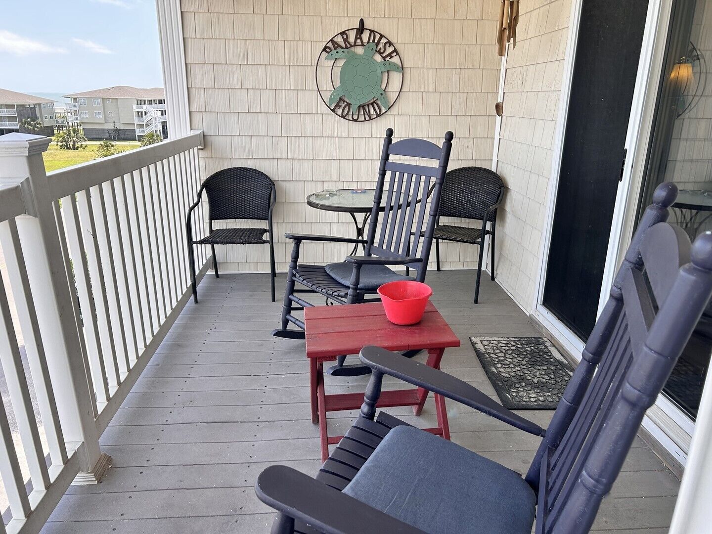 A balcony with two chairs, a small table, and a red bowl.