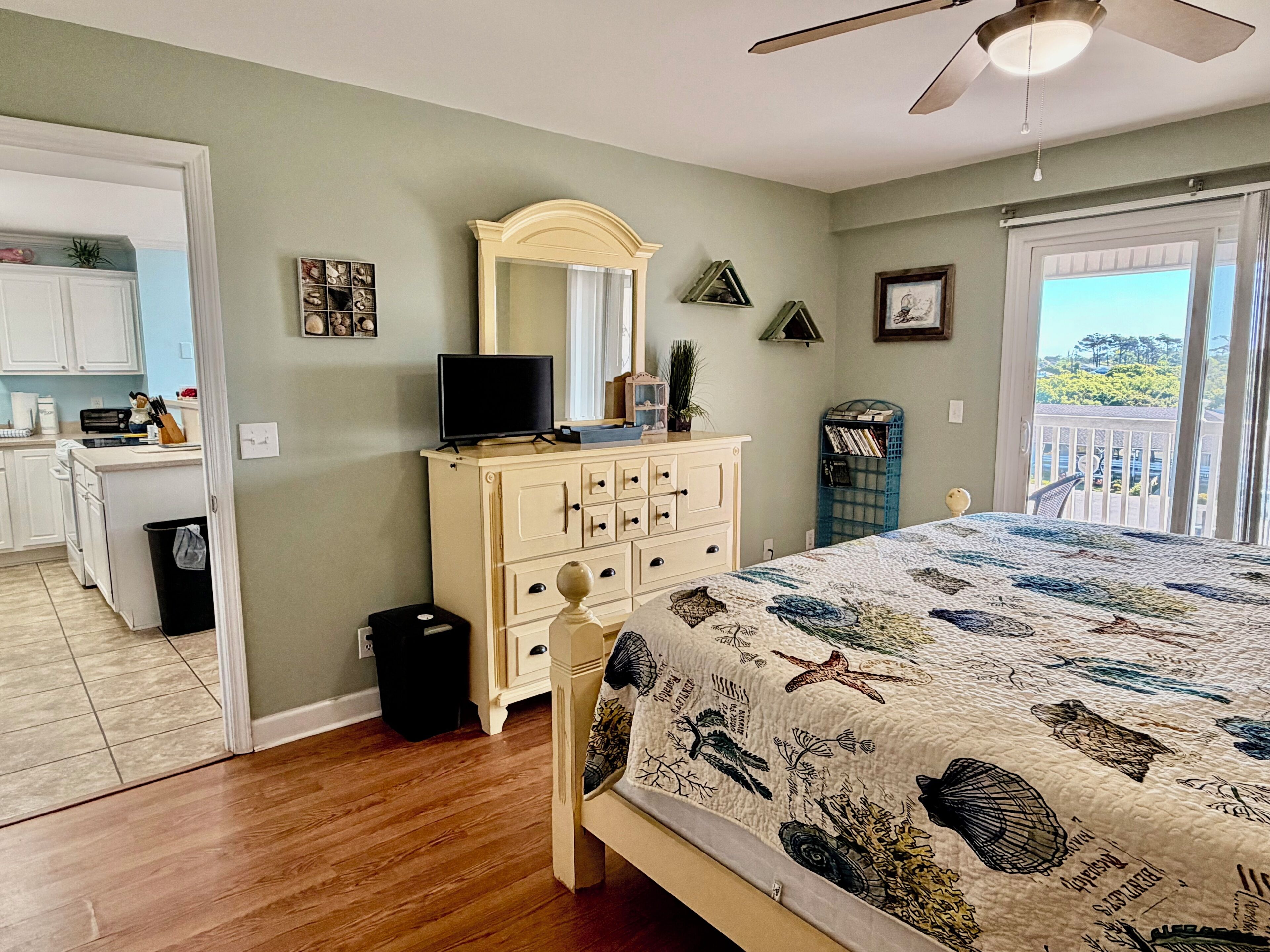 A bedroom with a bed, dresser, television, and a view of the outdoors.