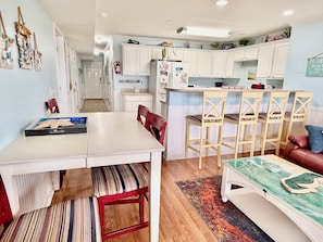 A compact kitchen with white cabinets, a dining area with a white table and chairs, and a living area with a sofa and a coffee table.
