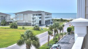 A multi-story building with a balcony, a grassy area with palm trees, and a view of the ocean. - Spacious oceanview condo in Oak Island, perfect for up to 9 guests with 3 bedrooms. (Oak Island)