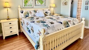 A bedroom with a bed, two nightstands, a ceiling fan, and a door leading to another room. - Spacious oceanview condo in Oak Island, perfect for up to 9 guests with 3 bedrooms. (Oak Island)
