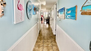 A hallway with artwork, a clock, and a view into a room with a table and chairs. - Spacious oceanview condo in Oak Island, perfect for up to 9 guests with 3 bedrooms. (Oak Island)